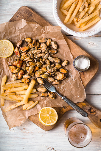 Mussels with lemons and French fries on the white wooden table vertical